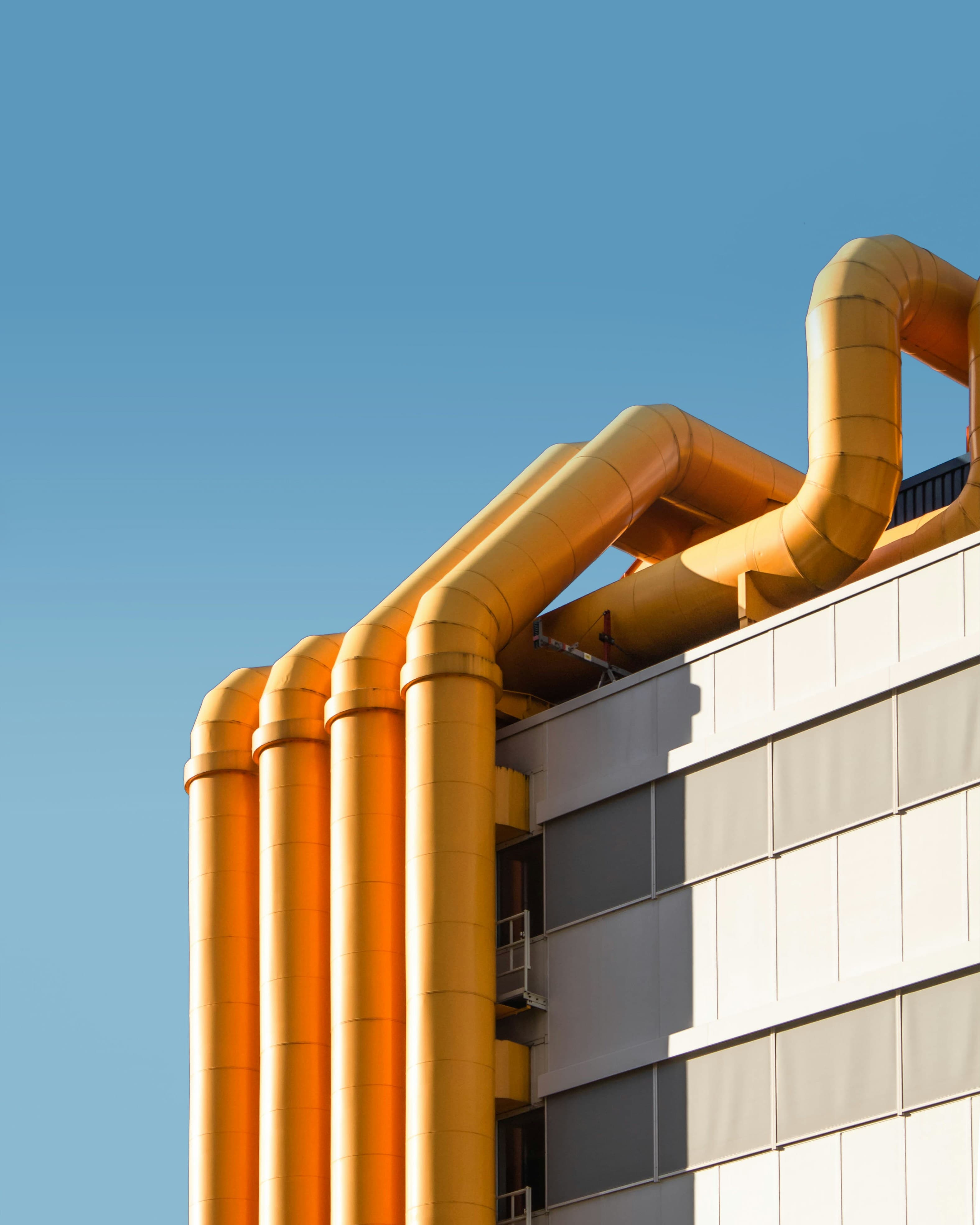 Bold orange industrial ducting against a clear blue sky